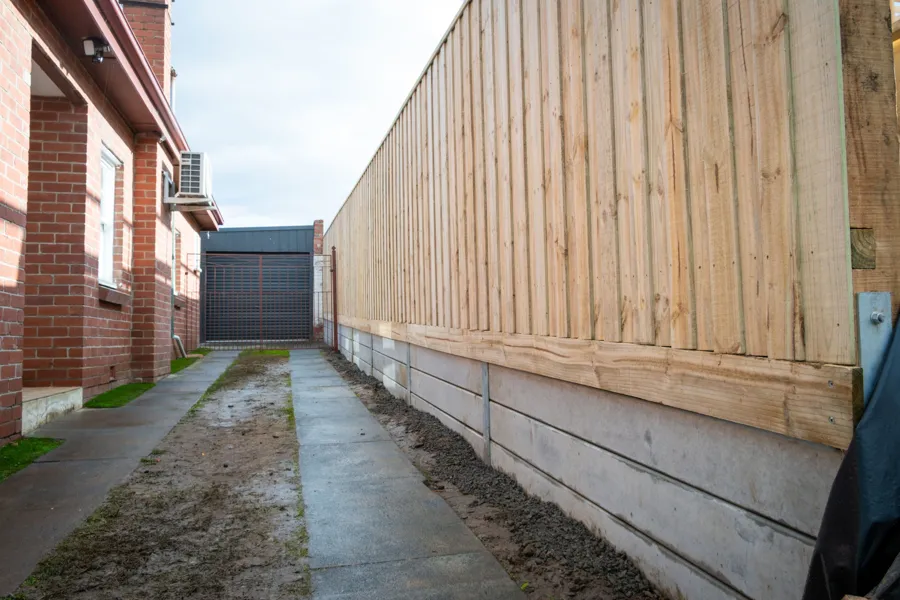 Long timber paling fence on concrete sleeper retaining wall along a driveway