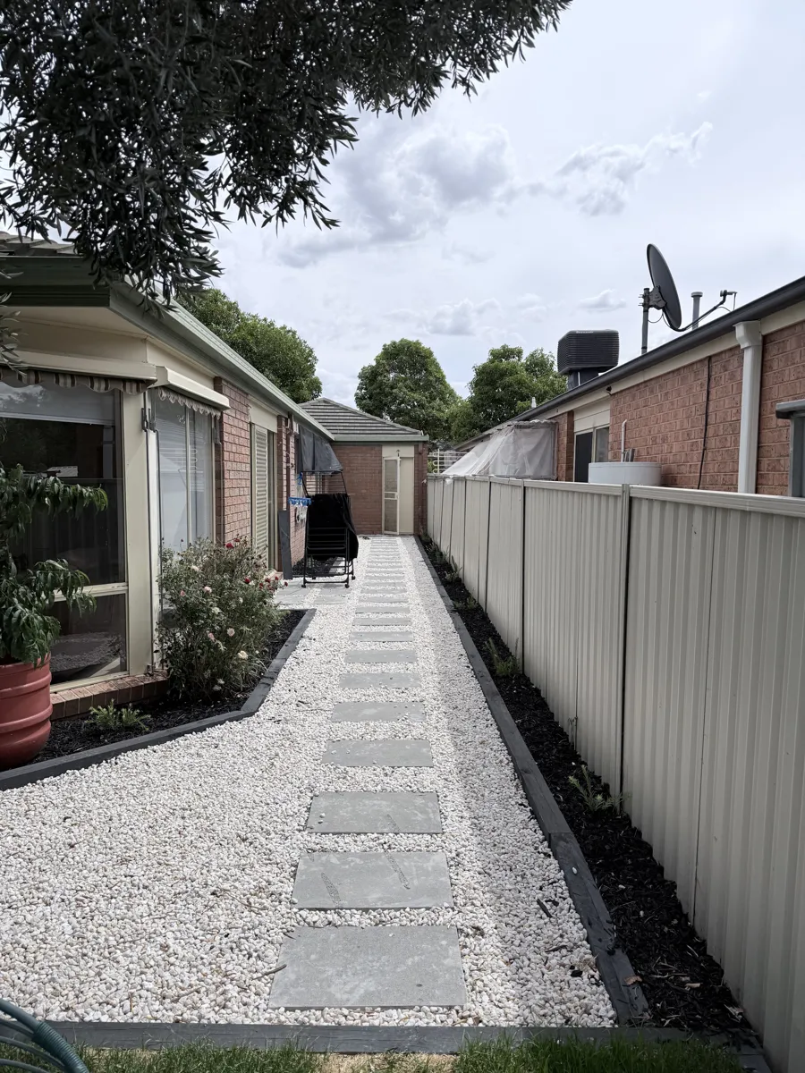 Stepping-stone path with edged garden beds beside a Colorbond fence